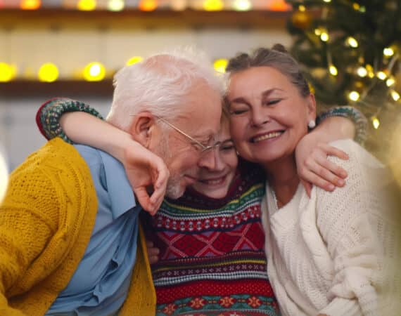 Smiling grandparents and grandson sitting on couch at home. Portrait of loving grandfather and grandmother embracing smiling preteen boy celebrating christmas together